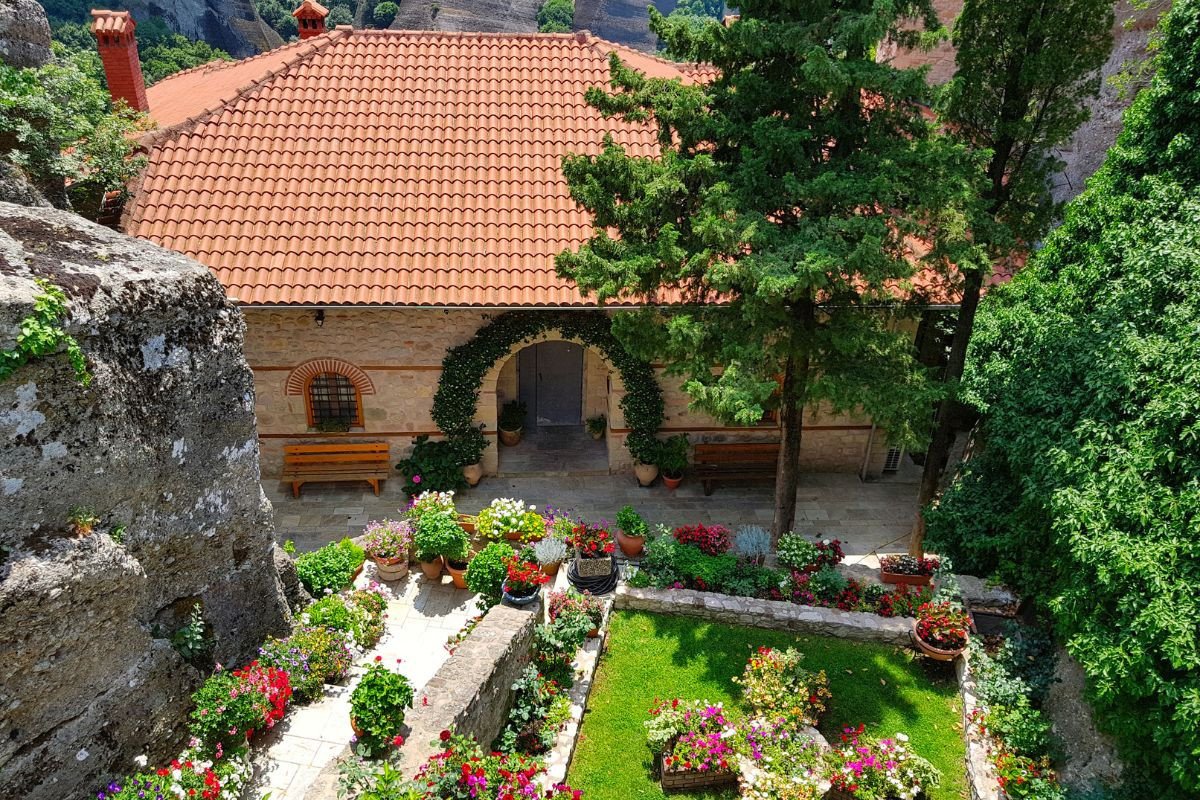 A courtyard garden with colorful flowers and greenery in front of a stone building with a red-tiled roof.